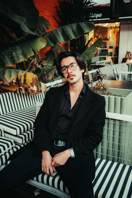 Free A fashionable young man in a black suit sitting in a stylish outdoor cafe environment. Stock Photo