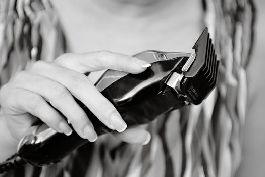 Black and white image of a hand holding an electric hair clipper, ideal for beauty and grooming themes.