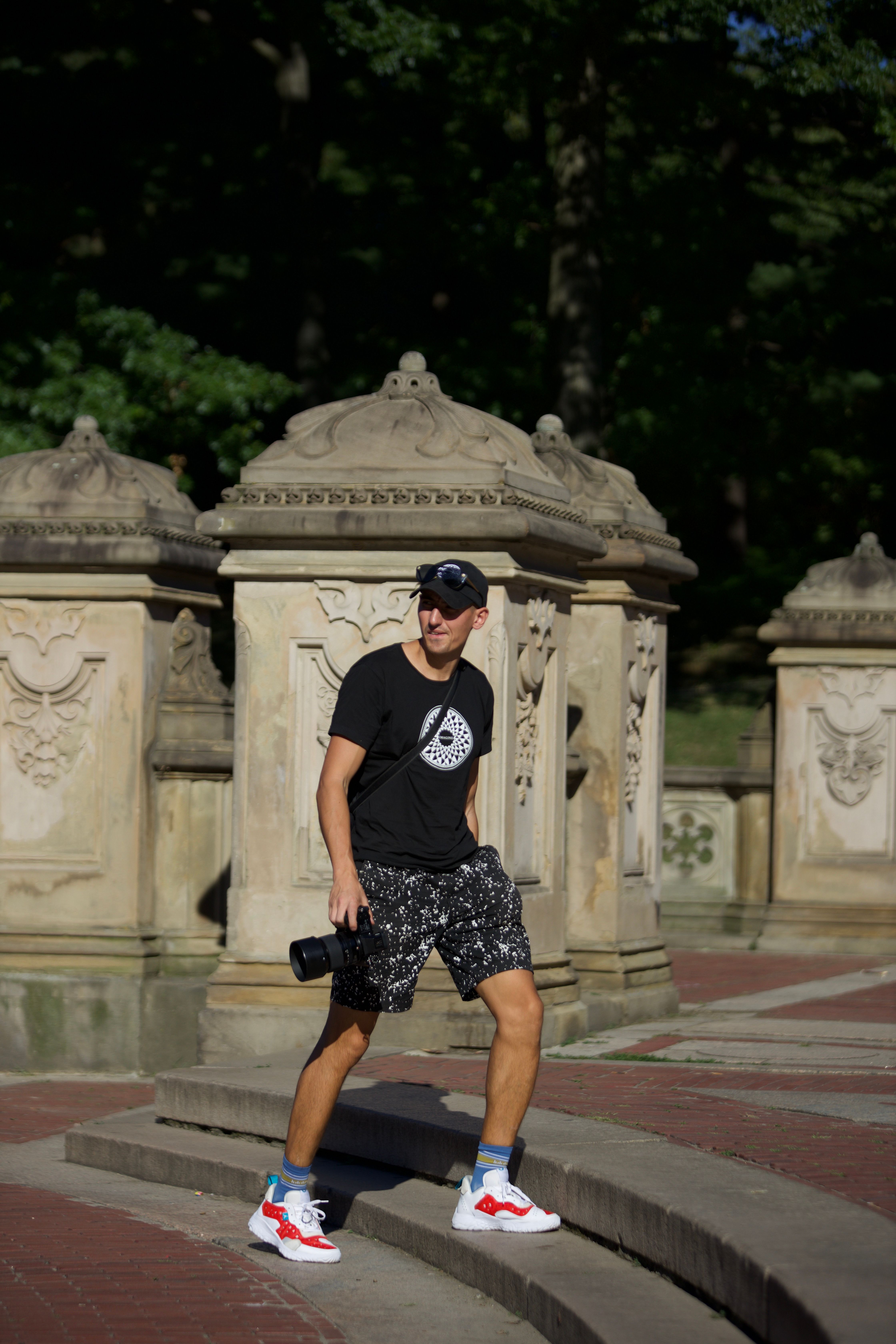 Man in urban park setting with camera, casual sporty outfit, bright day.