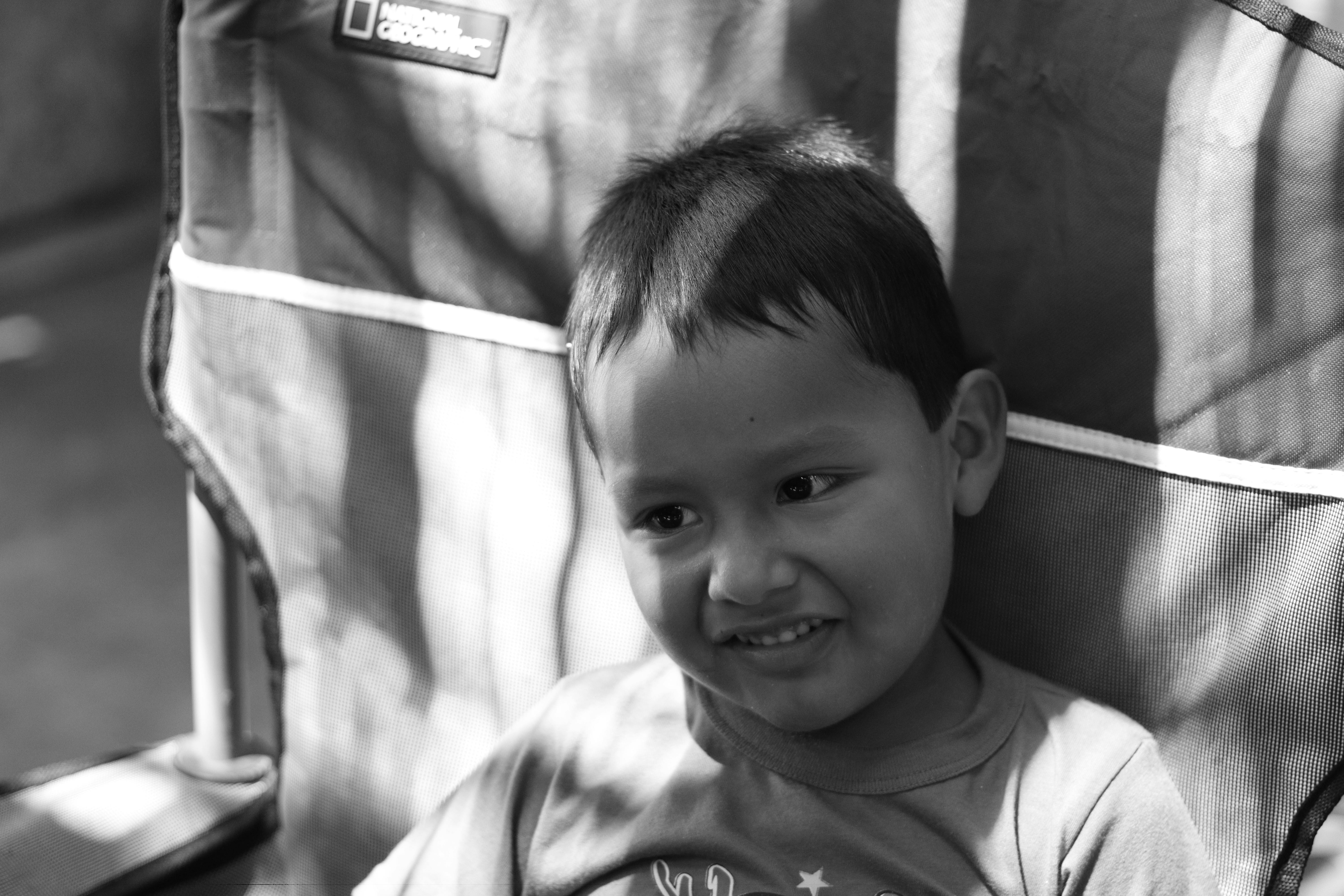 бесплатная Маленький ребенок улыбается, сидя на стуле в лучах заходящего солнца, снимок сделан на открытом воздухе. Стоковое фото