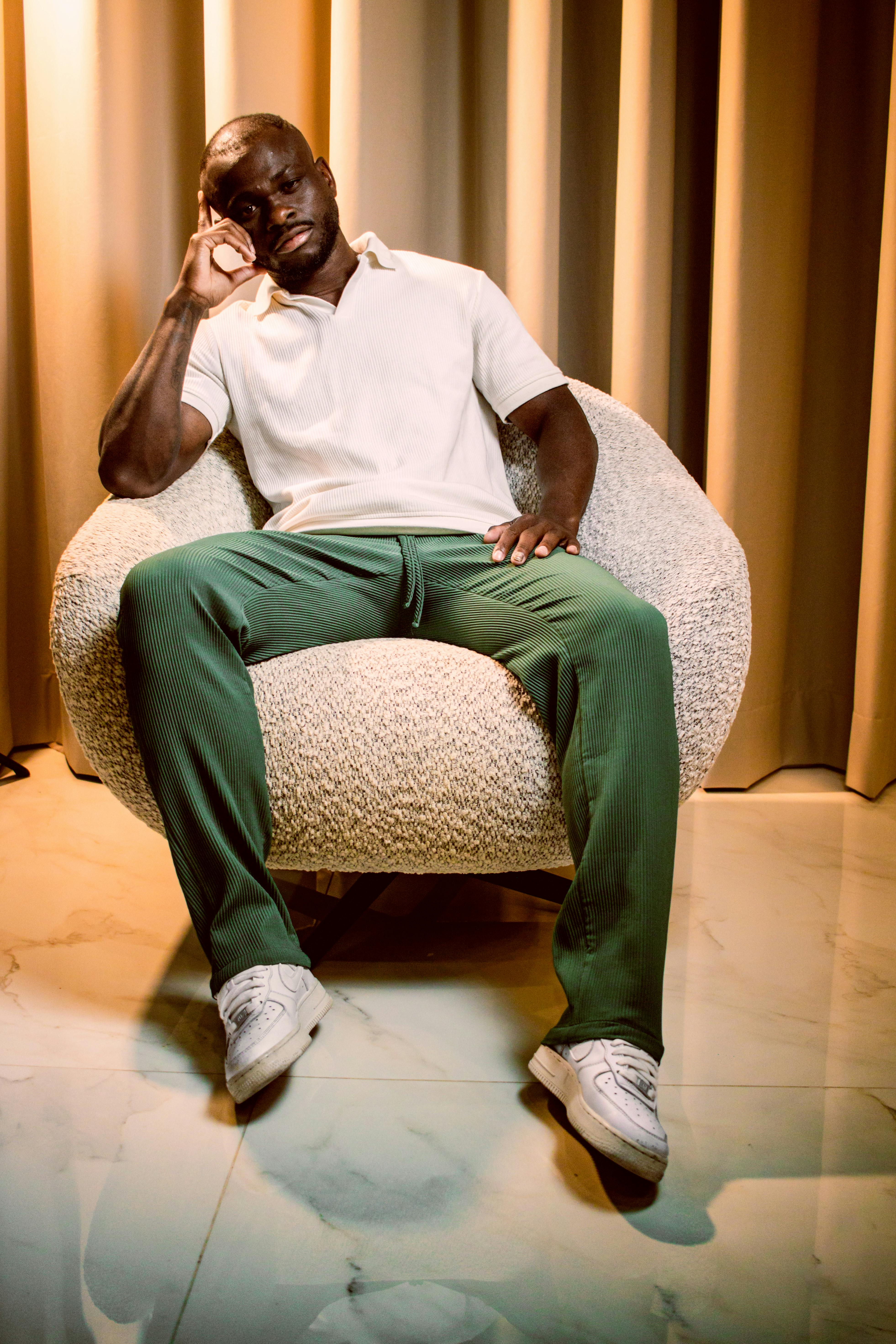 Kostnadsfria En elegant man i vardagskläder sitter avslappnat på en modern stol inomhus med elegant belysning. Stock foto