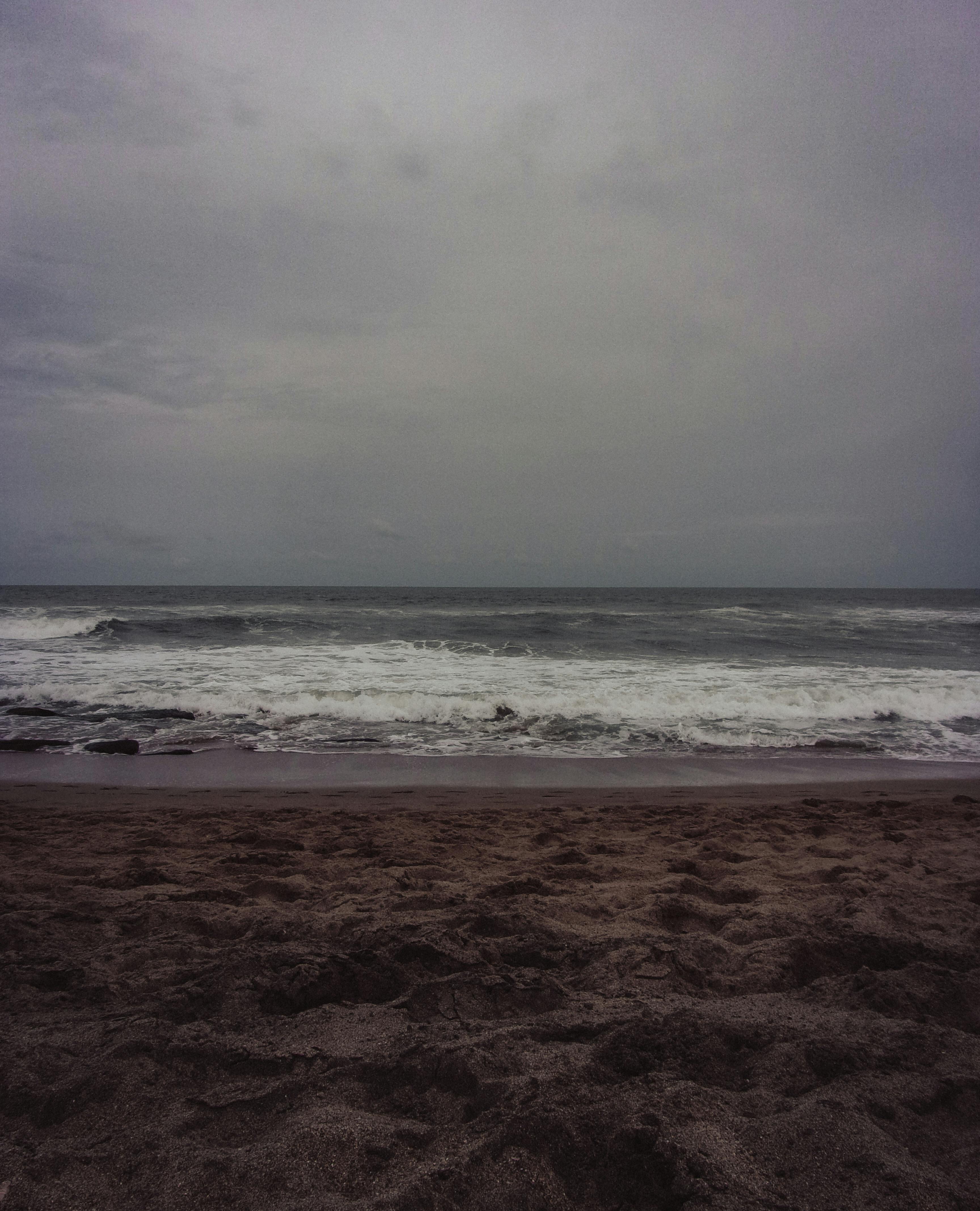 ingyenes Egy hangulatos tengerparti környezet borult éggel és megtörő hullámokkal, ami drámai hangulatot teremt. Stockfotó