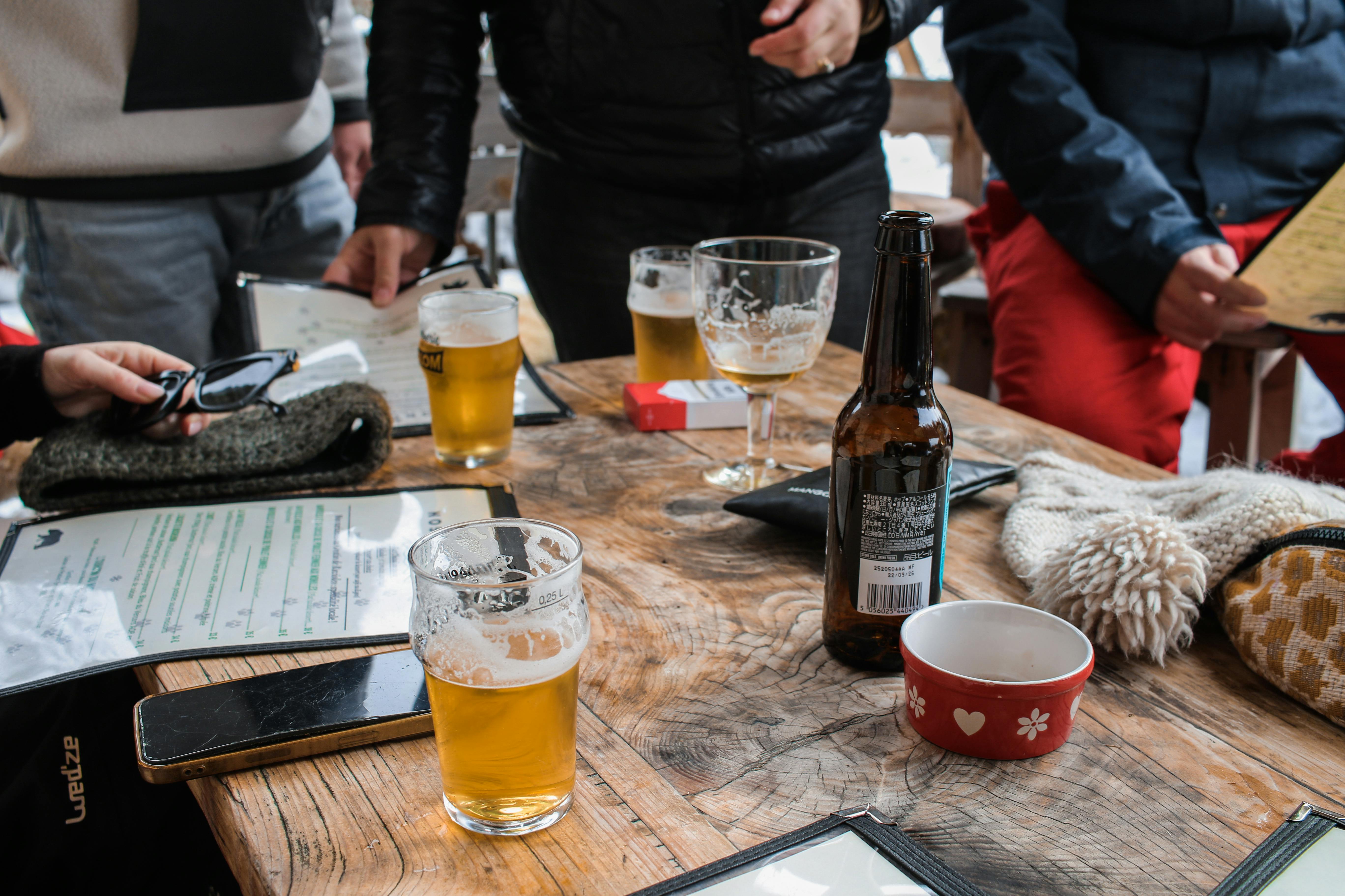 бесплатная Уютная встреча в помещении, где люди наслаждаются напитками и общаются за деревянным столом. Стоковое фото