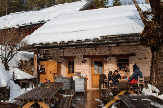 Charming winter cafe scene in Autrans-Méaudre-en-Vercors, France, with people enjoying outdoors.