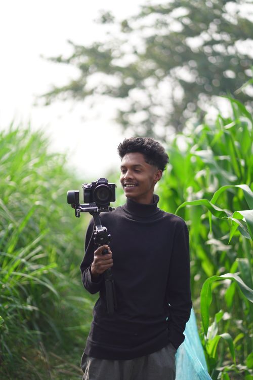 Free A happy young adult male photographer holding a camera on a gimbal in a lush green outdoor setting. Stock Photo