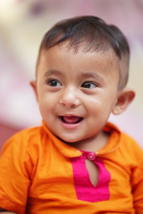 Free Cute baby smiling in an orange outfit, capturing joy and innocence. Stock Photo