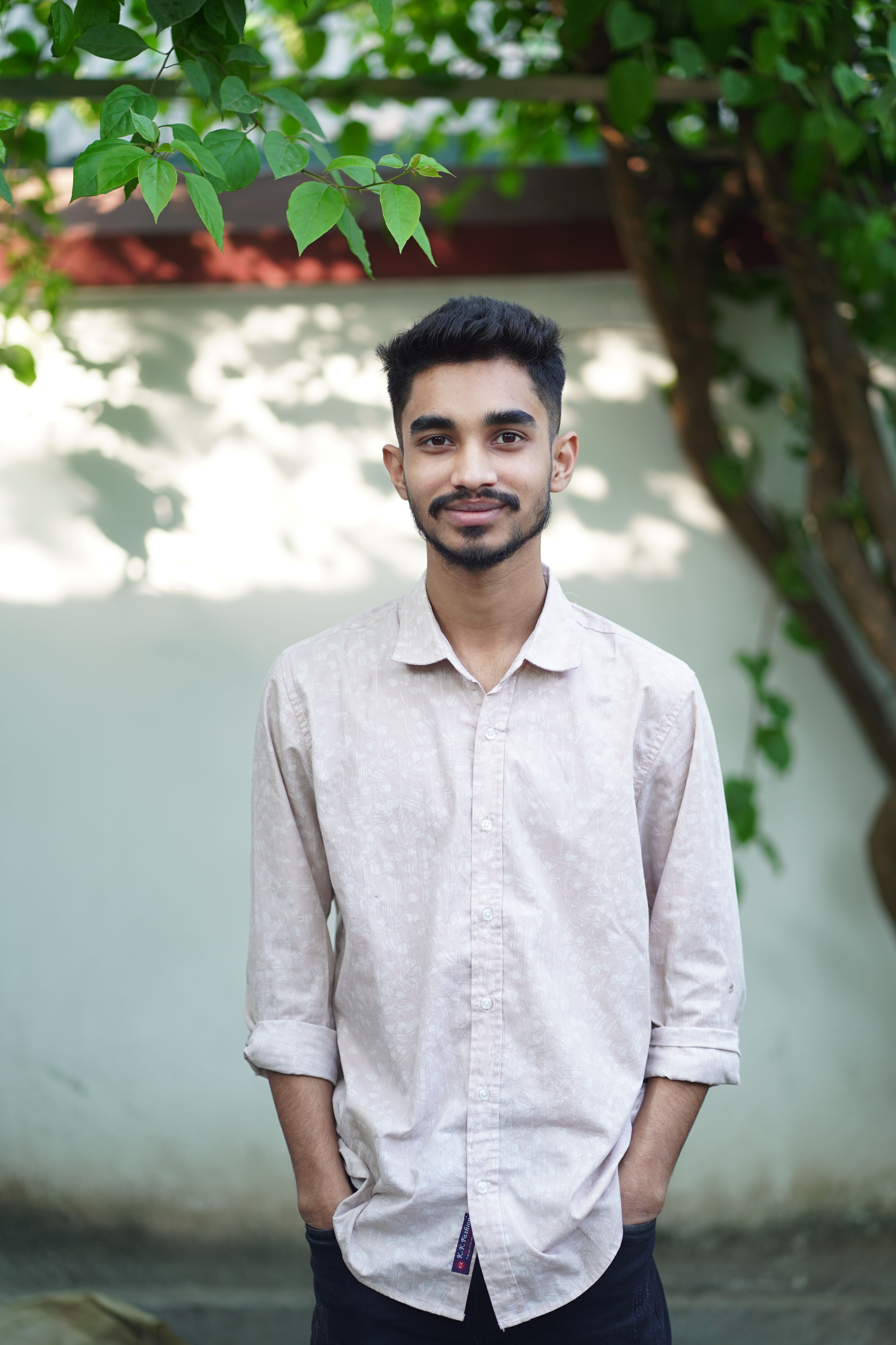 Portrait of a young man standing outside with a tree in the background on a sunny day.
