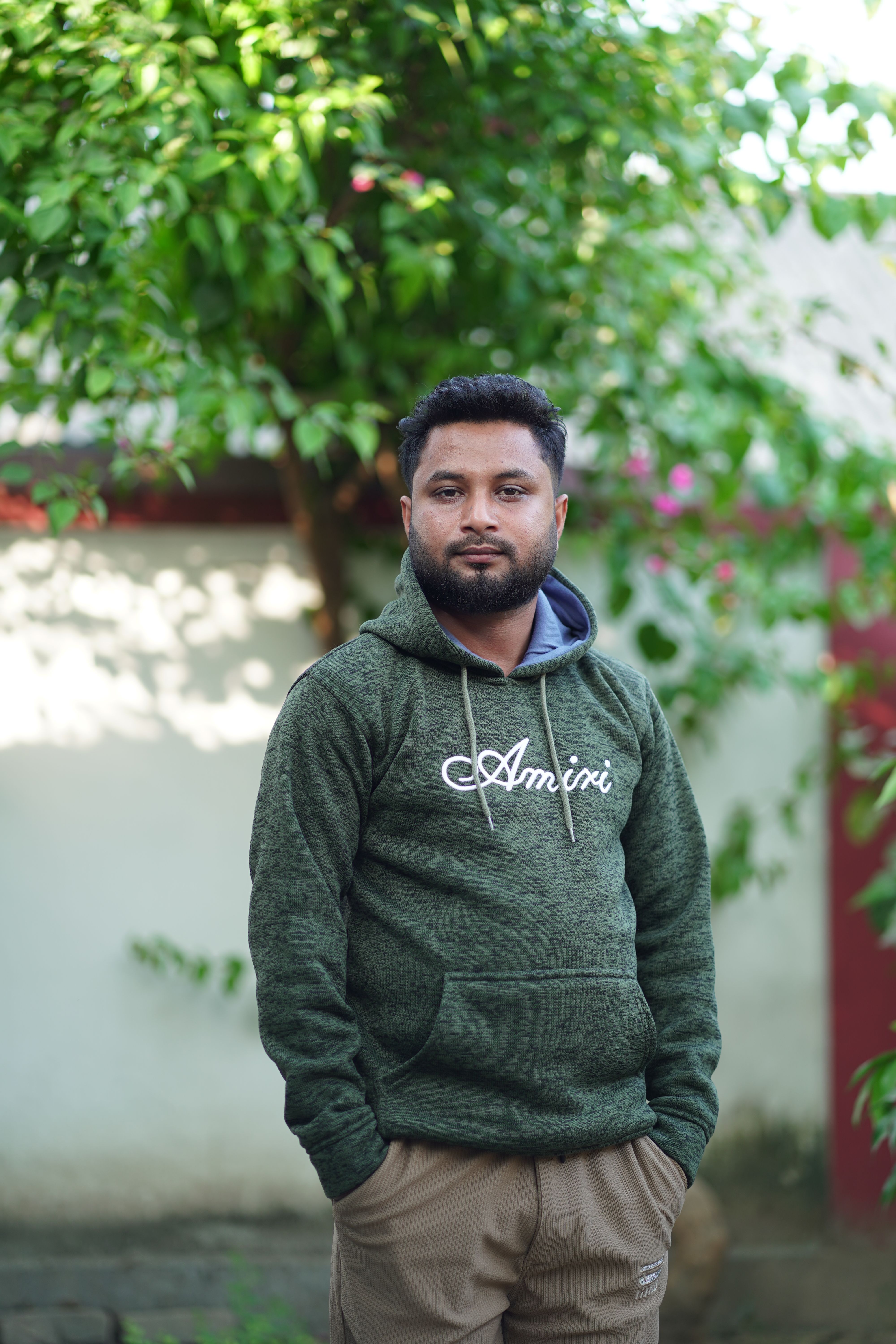 Portrait of a young man in a green hoodie standing outdoors in a garden setting.