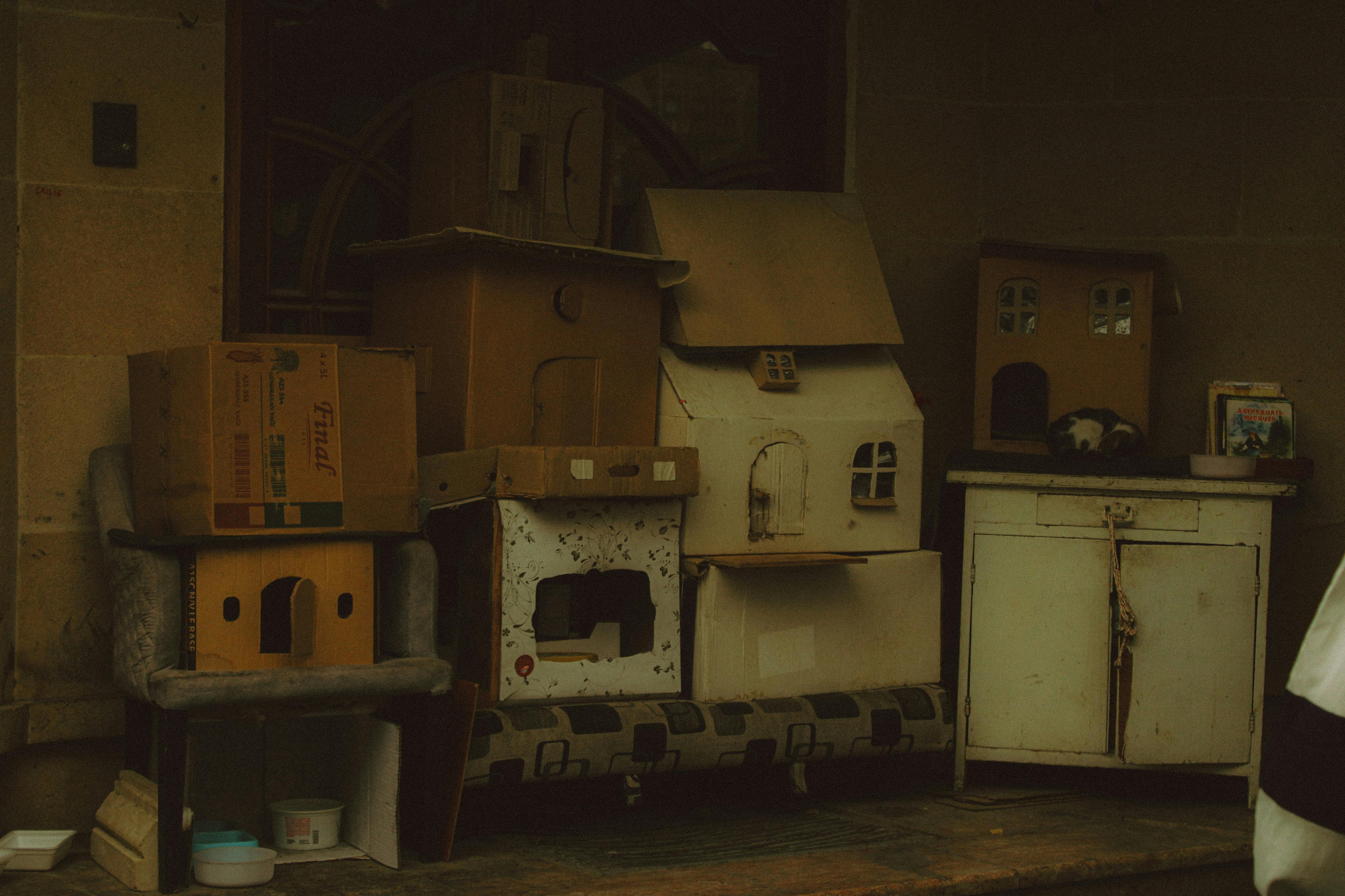 Kostenlos Eine Ansammlung selbstgebauter Katzenhäuser aus Pappe steht auf einer Veranda und bietet streunenden Katzen Unterschlupf. Stock-Foto