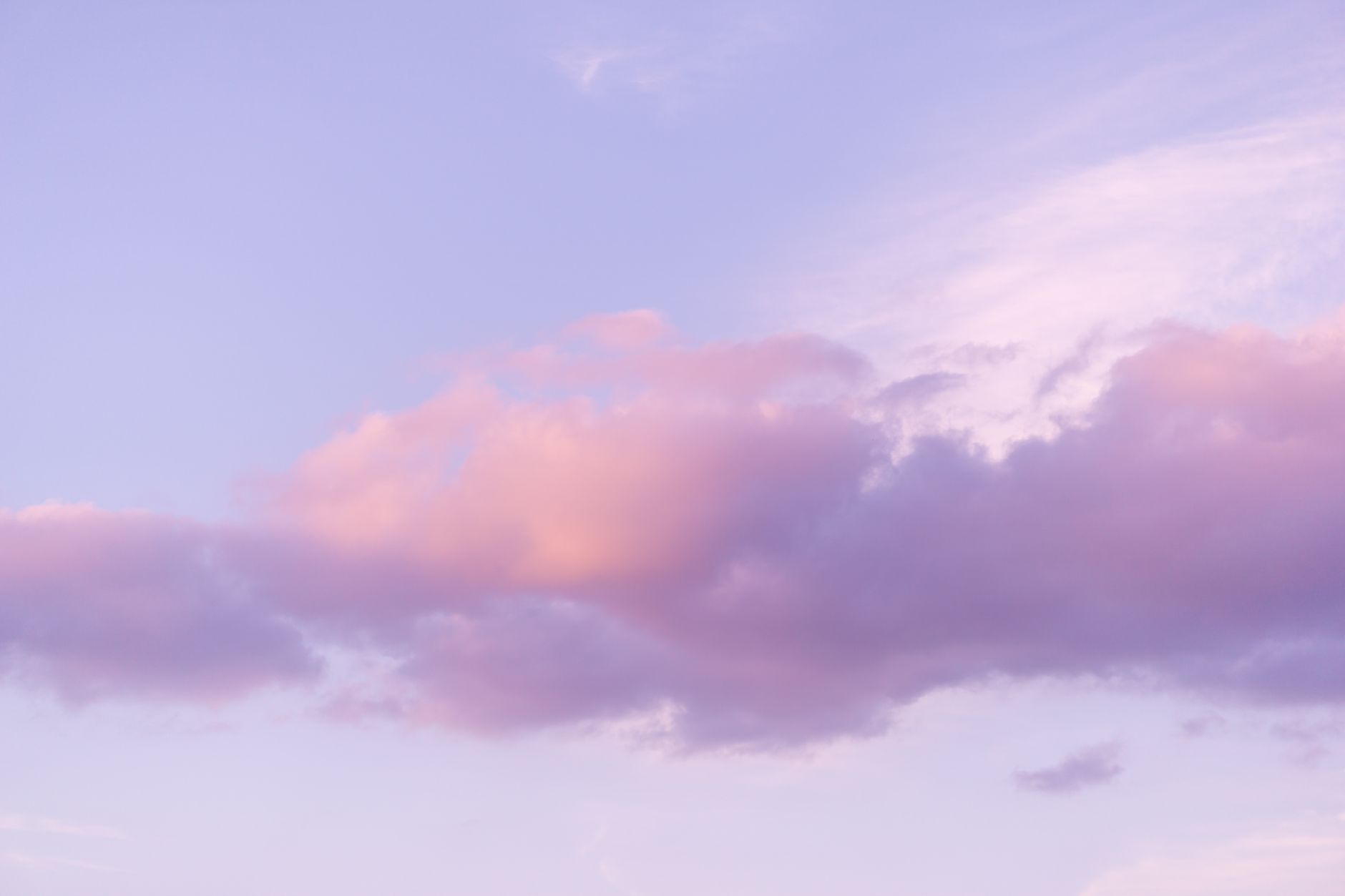 A calming view of pink and purple clouds floating in a clear sky during sunset.