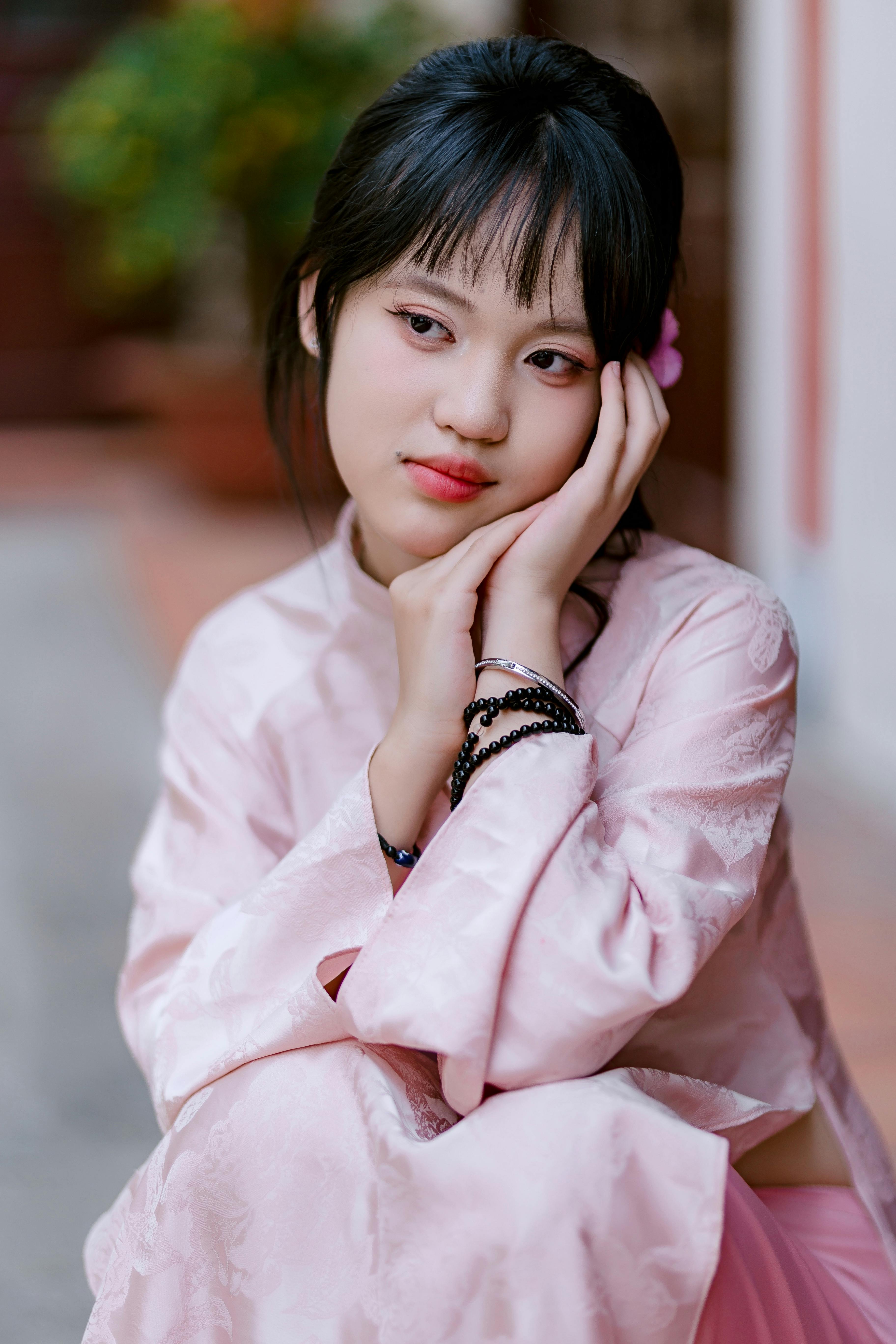 A young woman in traditional pink attire, sitting pensively outdoors.