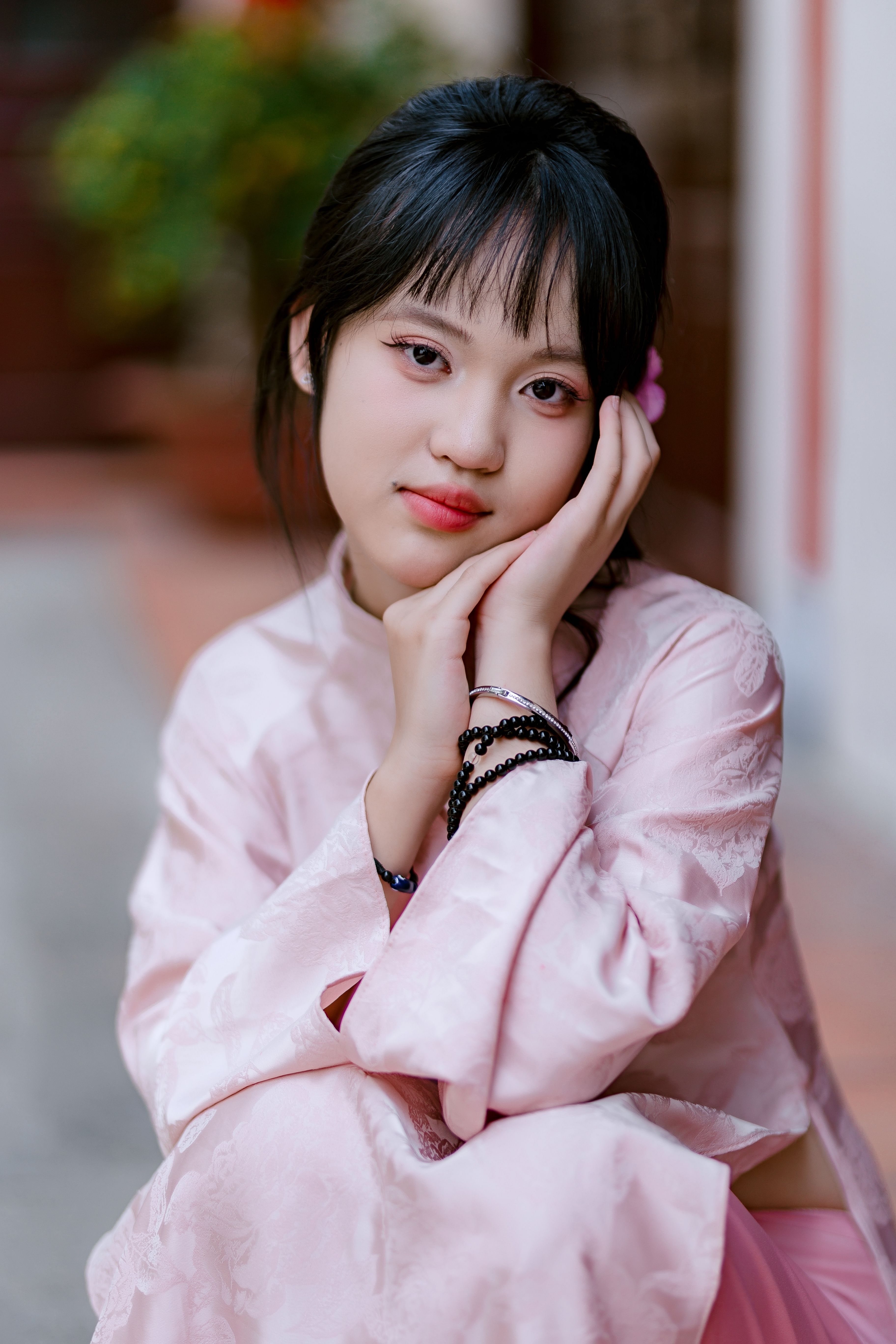 A serene portrait of a young woman in a traditional pink outfit, sitting indoors.