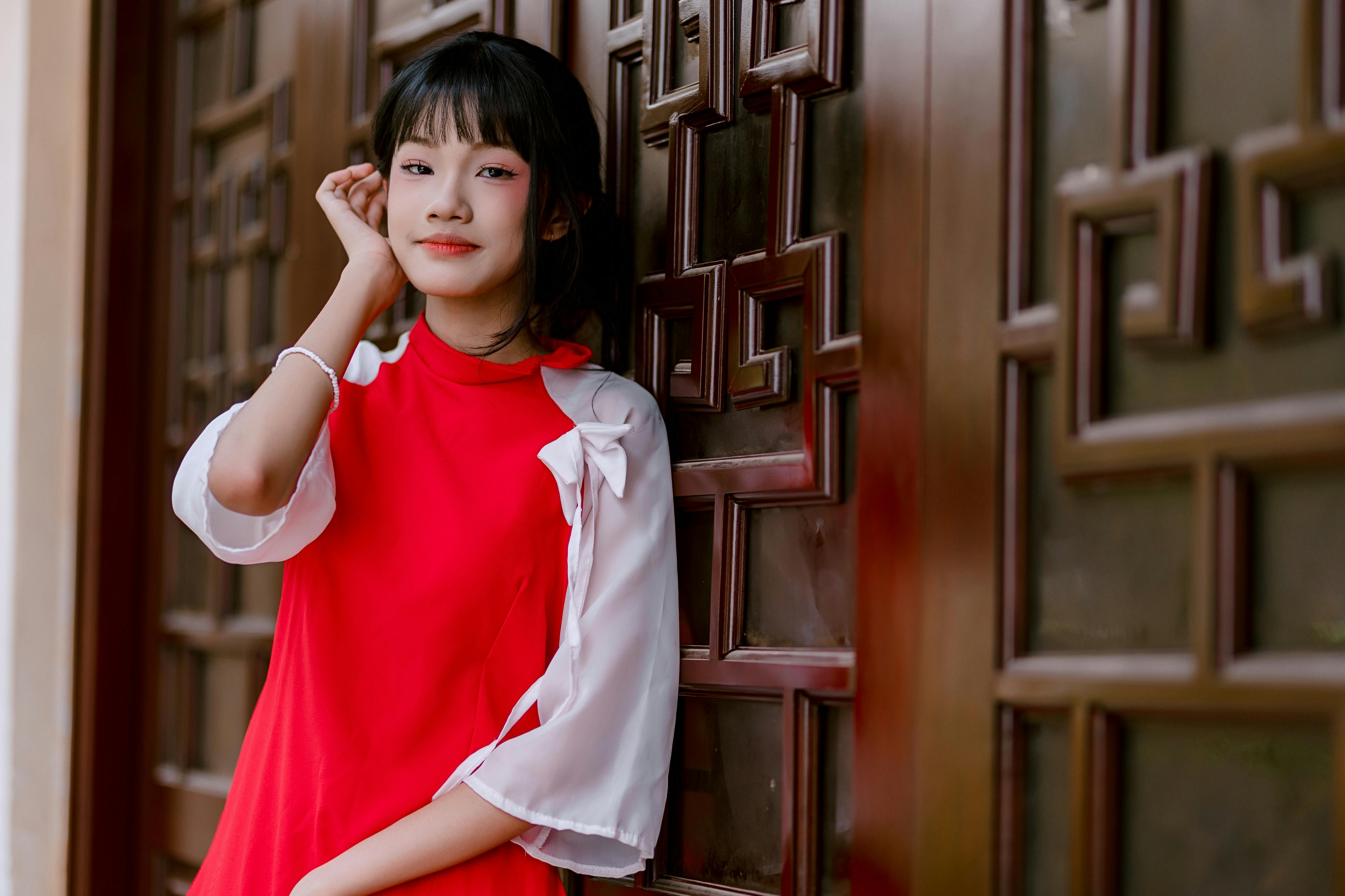 De franc Retrat d'una dona jove amb un vestit vermell recolzada casualment contra una paret de fusta estampada. Foto d'estoc