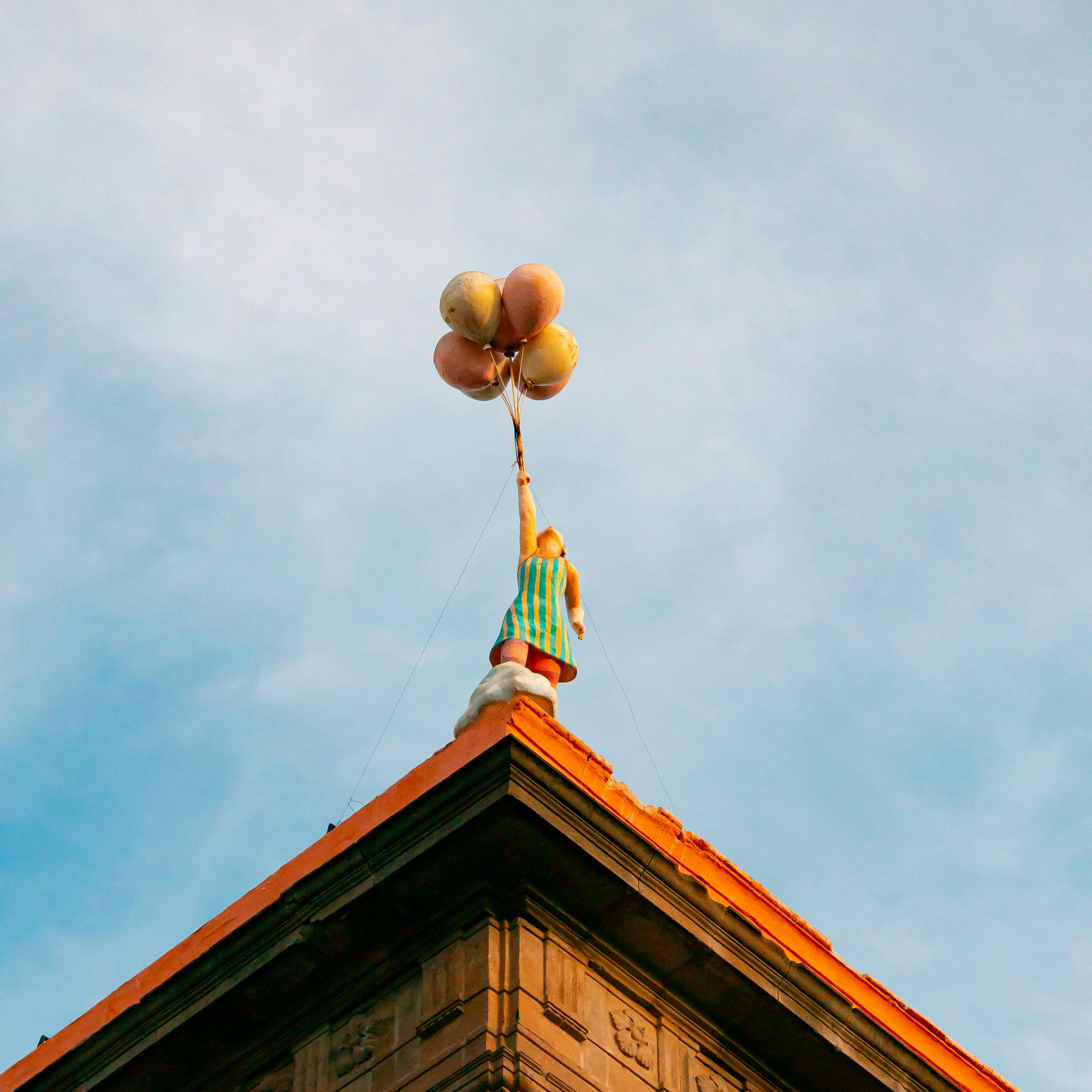 A whimsical child statue reaching for balloons atop a building in San Luis Potosí, Mexico.