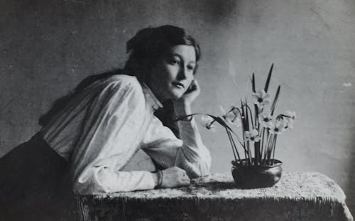 Woman in White Dress Shirt Leaning on Table With Flower Vase