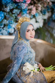 A beautiful bride in traditional Indonesian wedding dress with floral backdrop in Kendari.