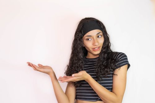 Free A young woman in a striped shirt confidently gestures against a white background. Stock Photo