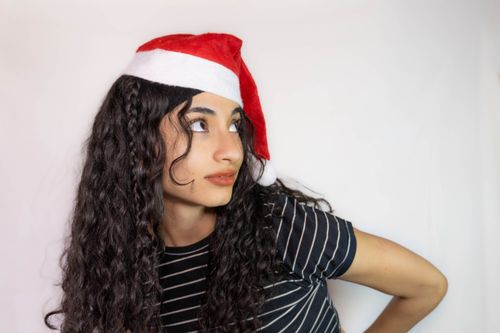 Free A young woman with curly hair wearing a Santa hat, looking sideways against a white background. Stock Photo