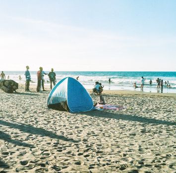 A vibrant beach scene with people enjoying the sun and waves, featuring a prominent tent.