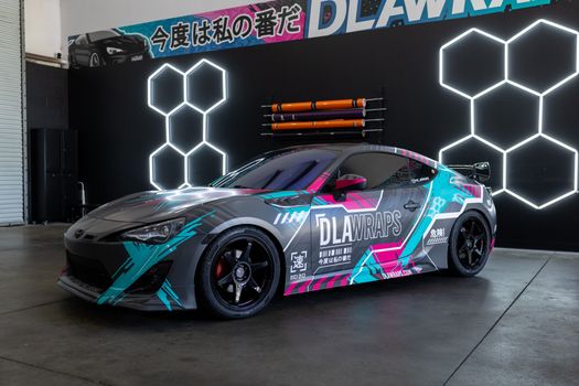 Dynamic photo of a sleek sports car with colorful custom vinyl wrap by DLA Wraps in a shop setting.