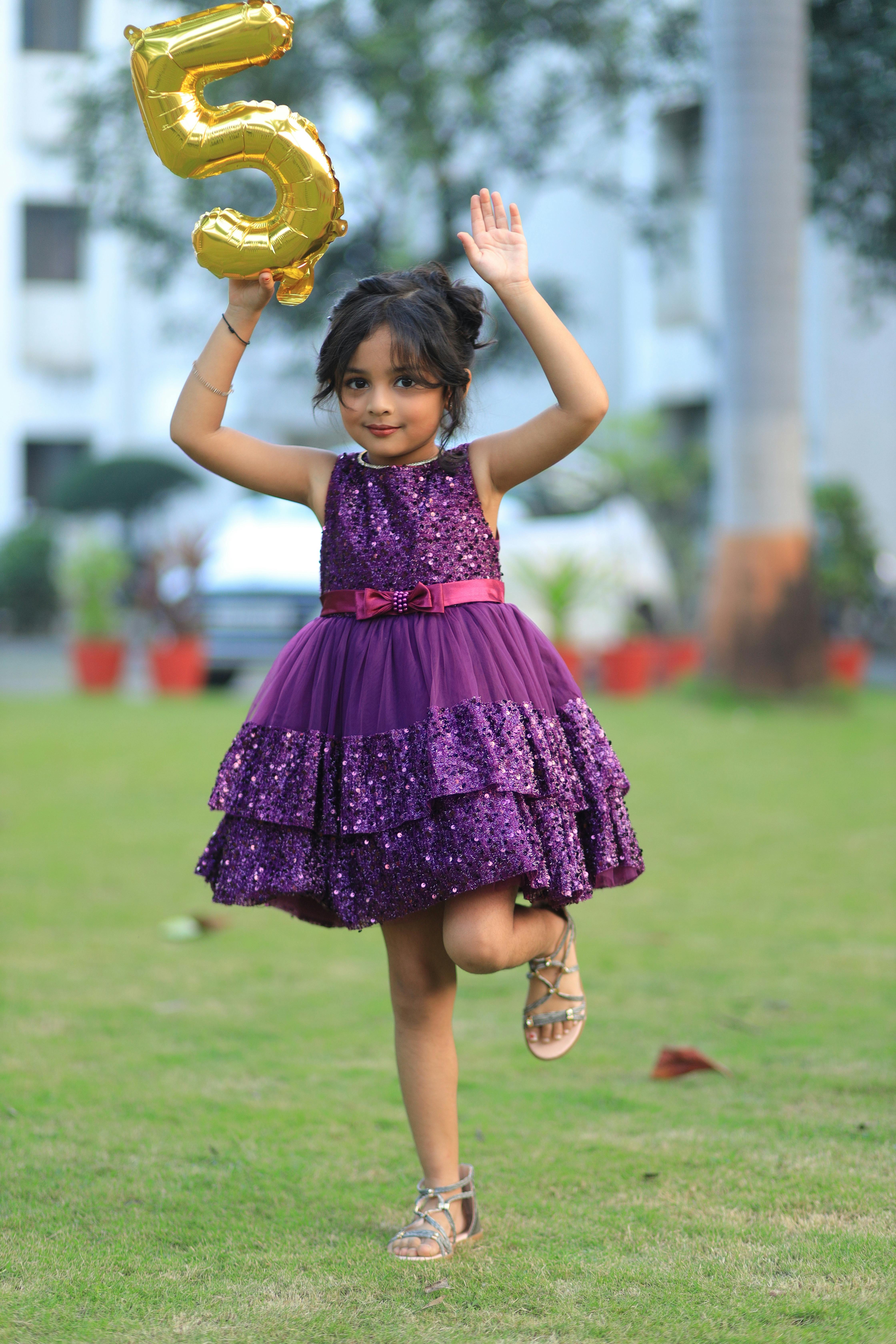 A young girl joyfully poses outdoors, celebrating her fifth birthday with a balloon.