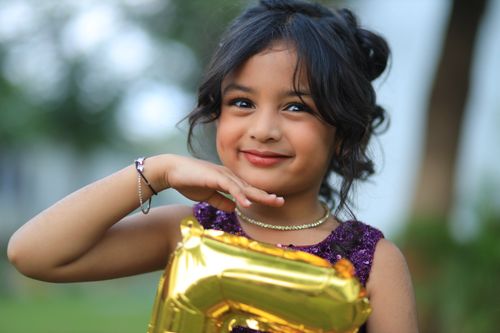 Free Adorable child smiling while holding a golden number balloon, outdoors in a playful setting. Stock Photo