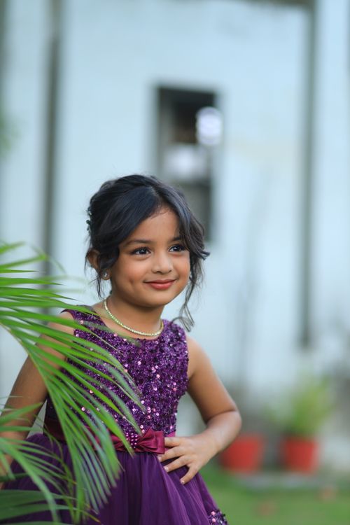 Free Delightful outdoor portrait of a smiling young girl in a purple dress amidst greenery. Stock Photo