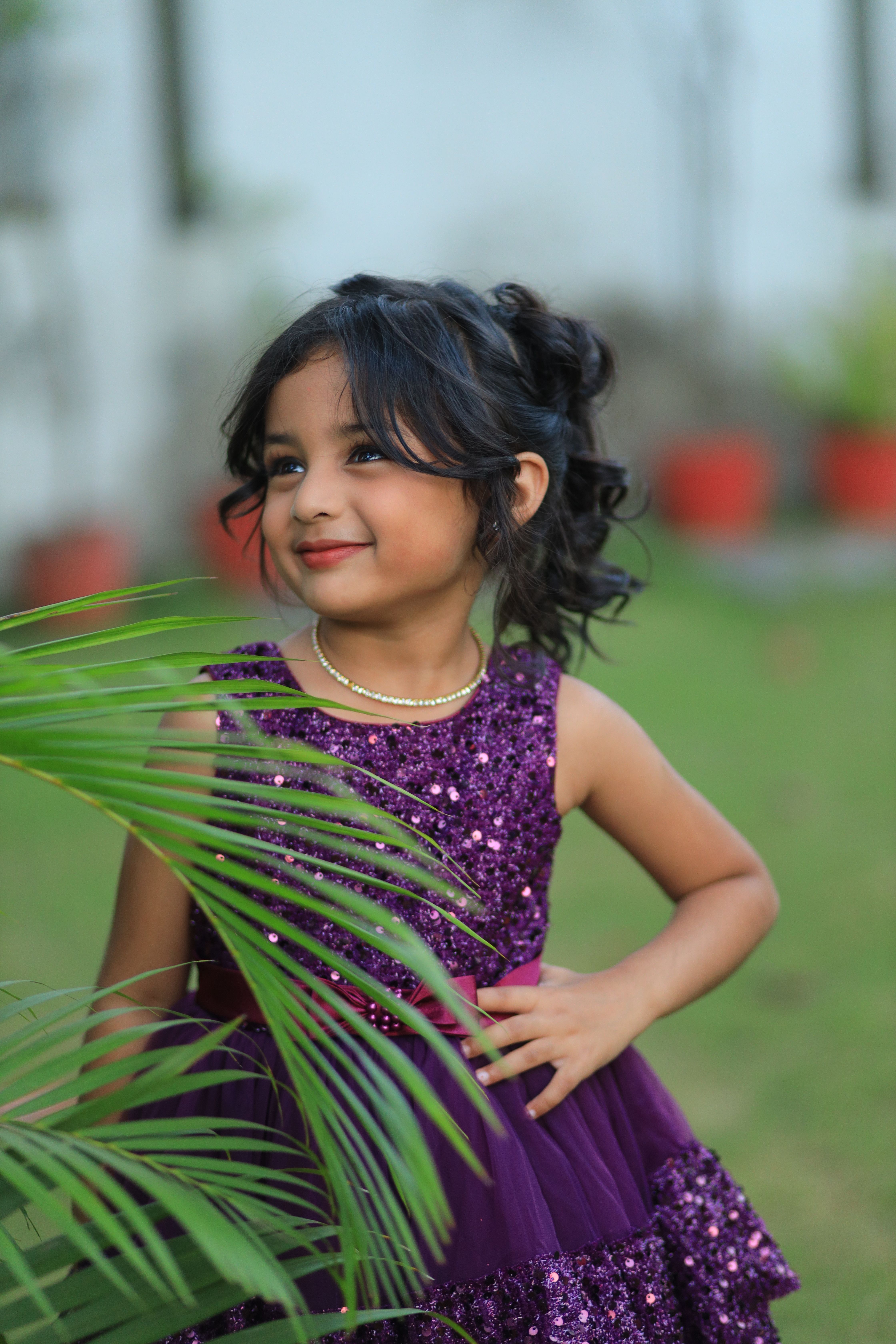 Adorable child in a sparkly purple dress enjoying a sunny day outdoors.