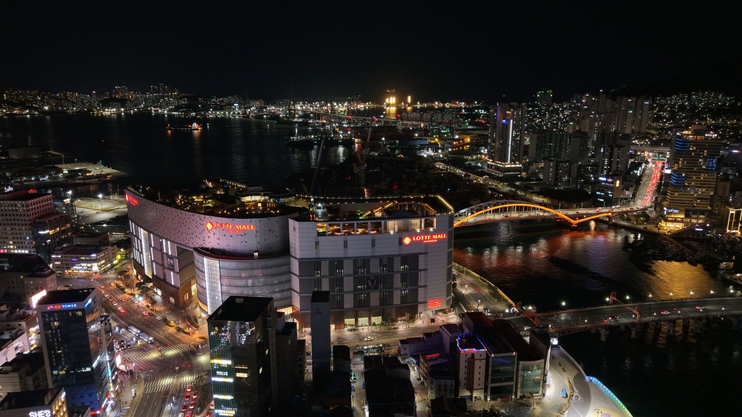 Aerial night view of Busan, South Korea featuring Lotte Mall and iconic bridges.