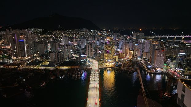 Stunning aerial shot of Busan cityscape at night, featuring illuminated skyscrapers and a bridge.