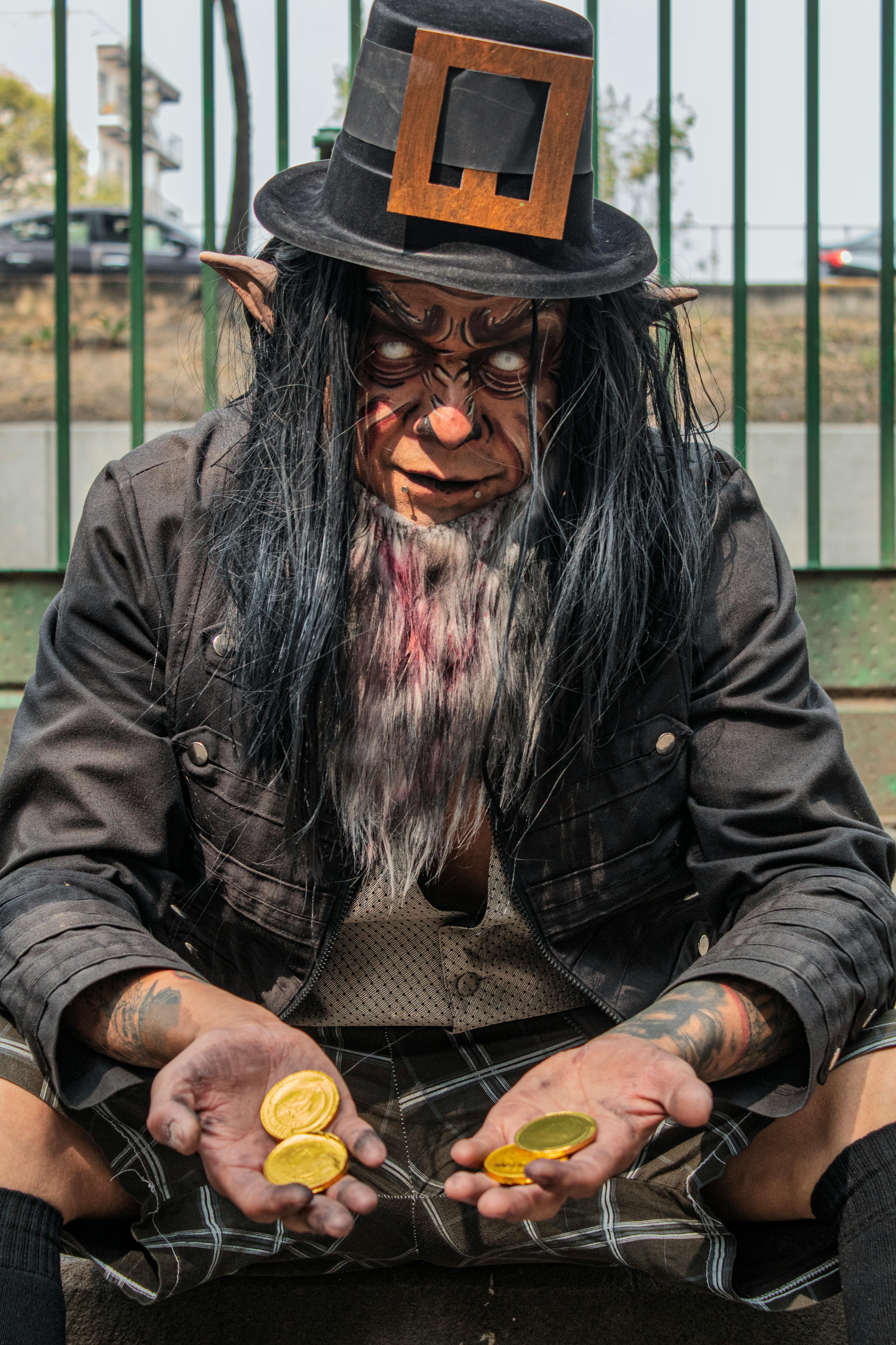 Gratis Un artista in costume vestito da creatura mistica, che tiene in mano monete d'oro all'aperto. Foto a disposizione