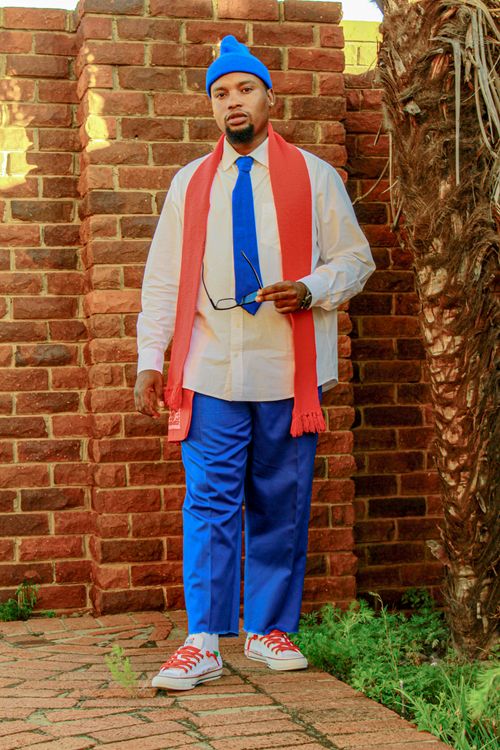 Free Stylish man wearing a bright blue and red outfit poses against a brick wall outdoors. Stock Photo