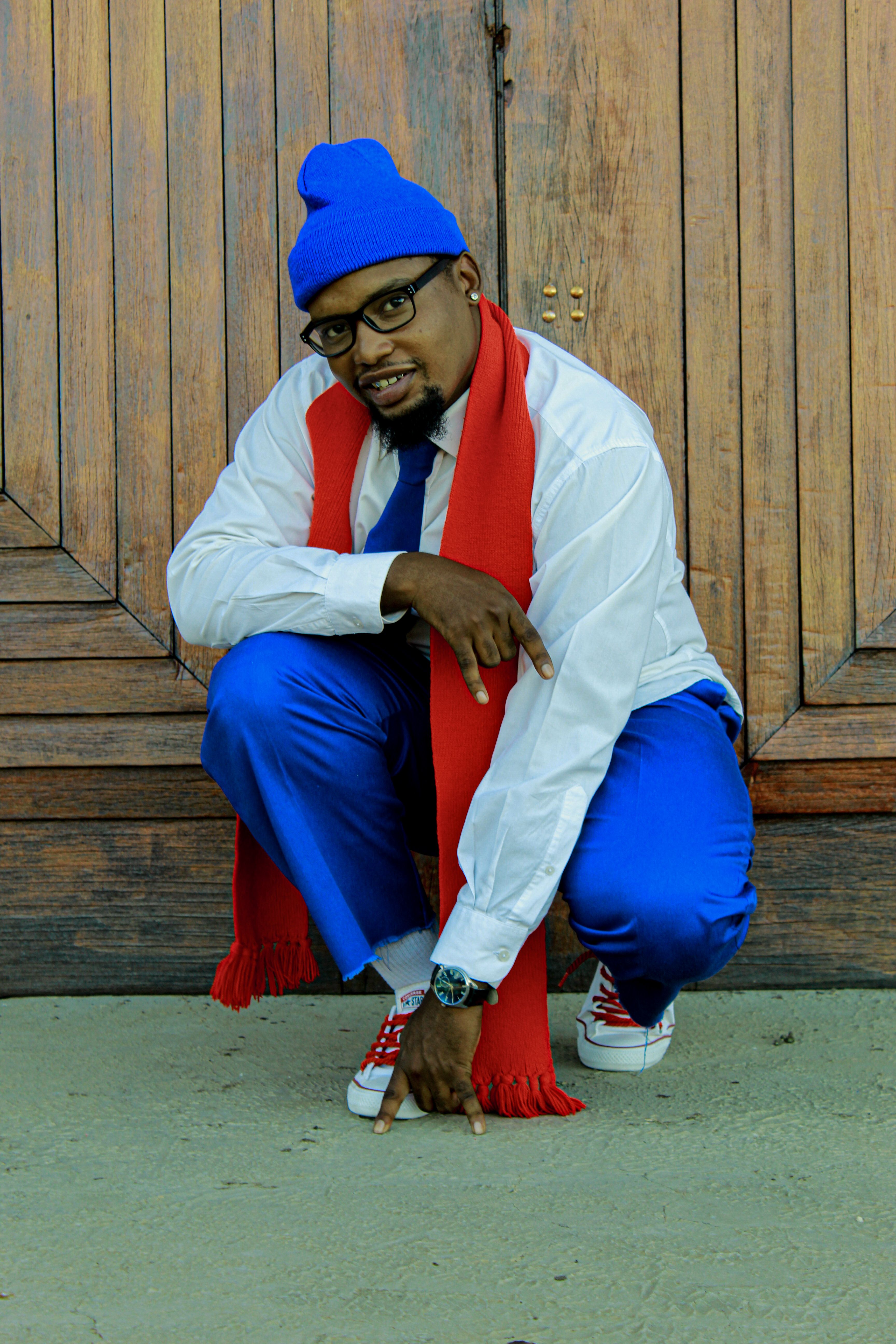 A fashionable man in a blue suit and red scarf poses confidently in front of a wooden door.