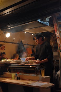 Street food vendor grilling in Shinjuku, Tokyo at night, capturing lively atmosphere.