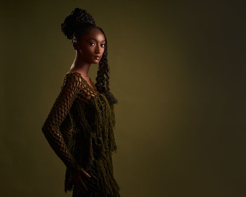 A stylish portrait capturing a woman in an artistic, fringed outfit against a muted background.