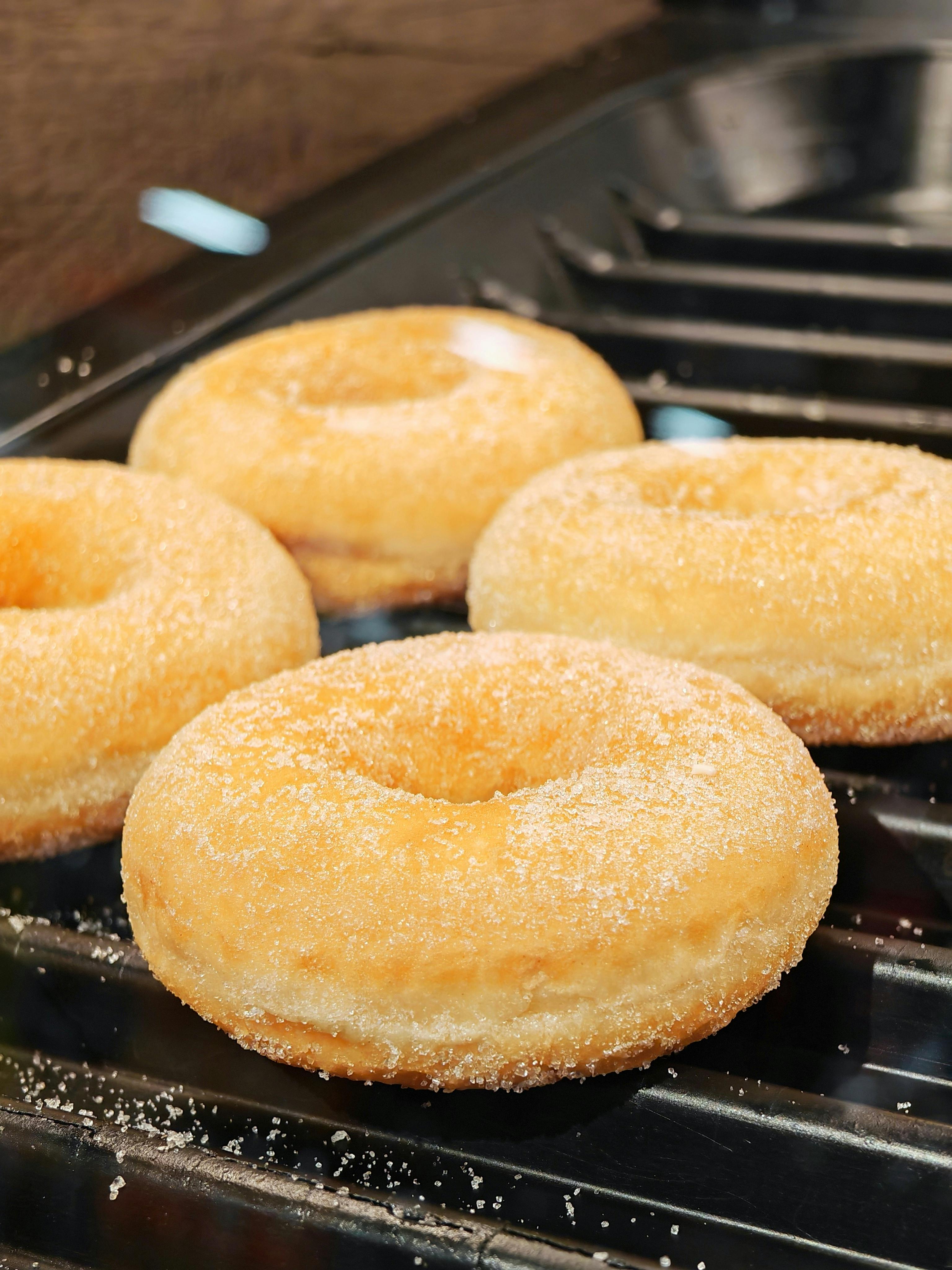 Close-up of four sugar-coated donuts resting on a griddle, freshly made.