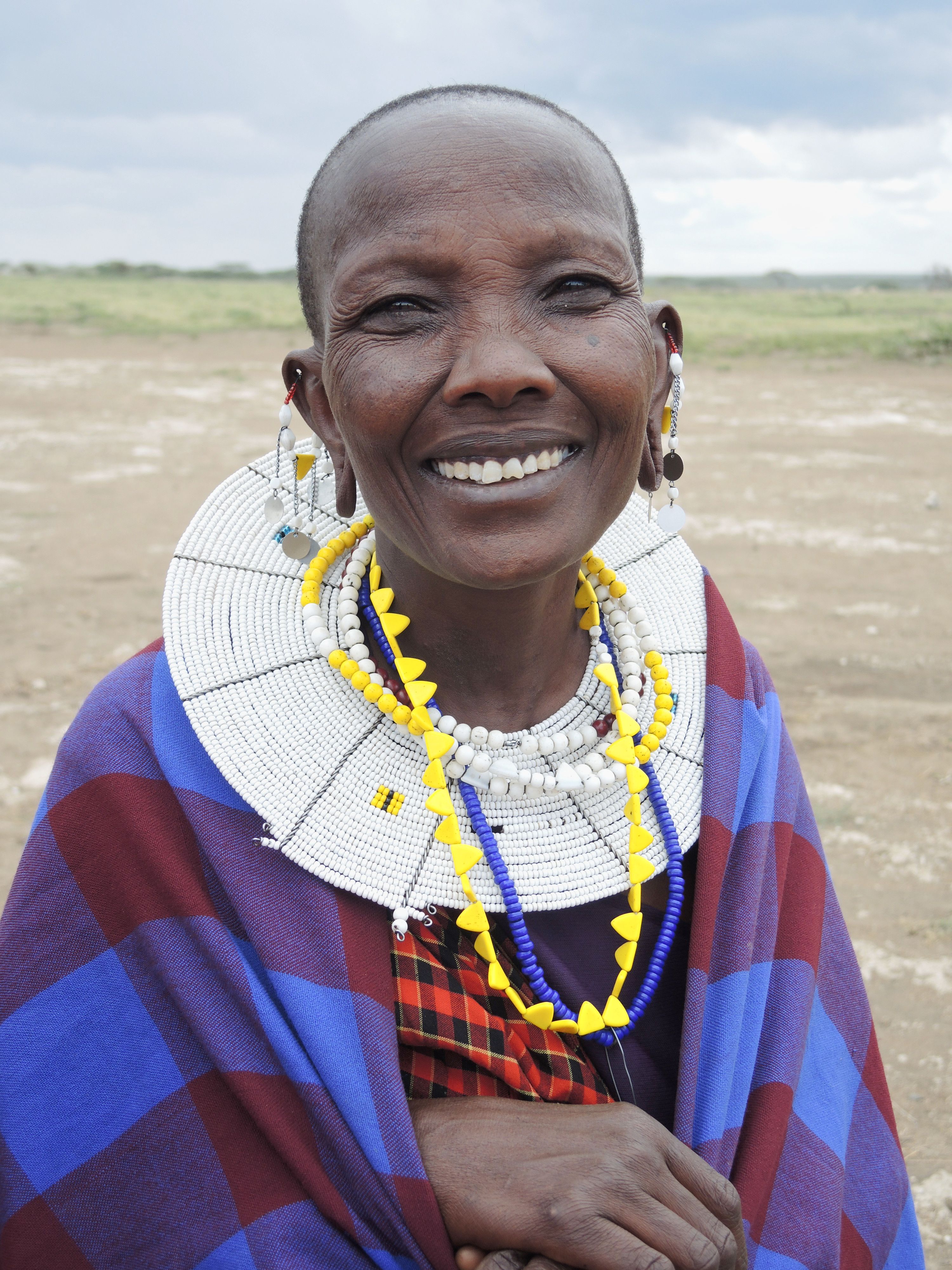 Smiling Maasai woman adorned in vibrant traditional beadwork and clothing, outdoors.