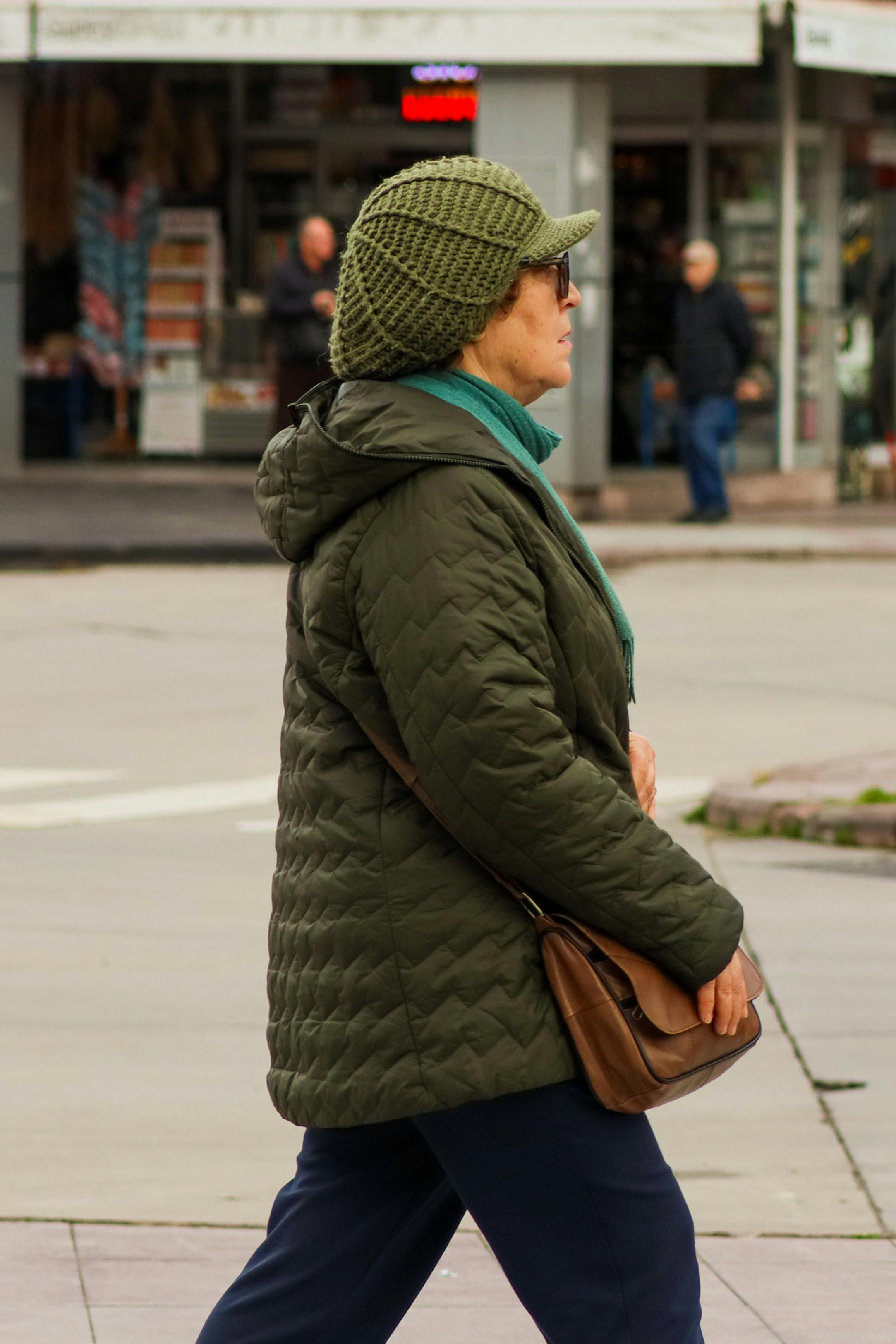 Bezpłatne Widok z boku na kobietę w zimowym ubraniu spacerującą ulicą miasta. Zdjęcie z galerii