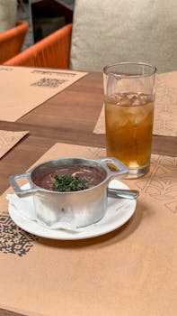Metal pot of feijoada with iced tea on a restaurant table setting.