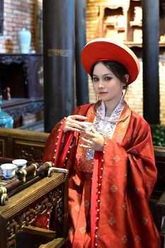 Woman in traditional Asian attire holding a tea cup in an ornate cultural setting.