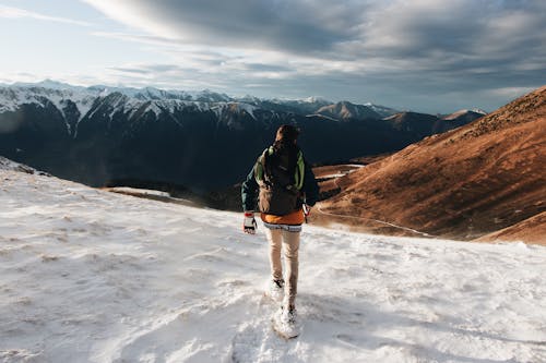 Man in Black Jacket and Blue Denim Jeans Walking on Snow Covered Ground