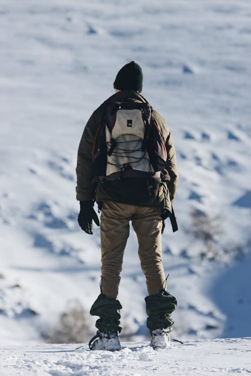 Unrecognizable traveler standing on snowy land against mountain ridge on sunny day