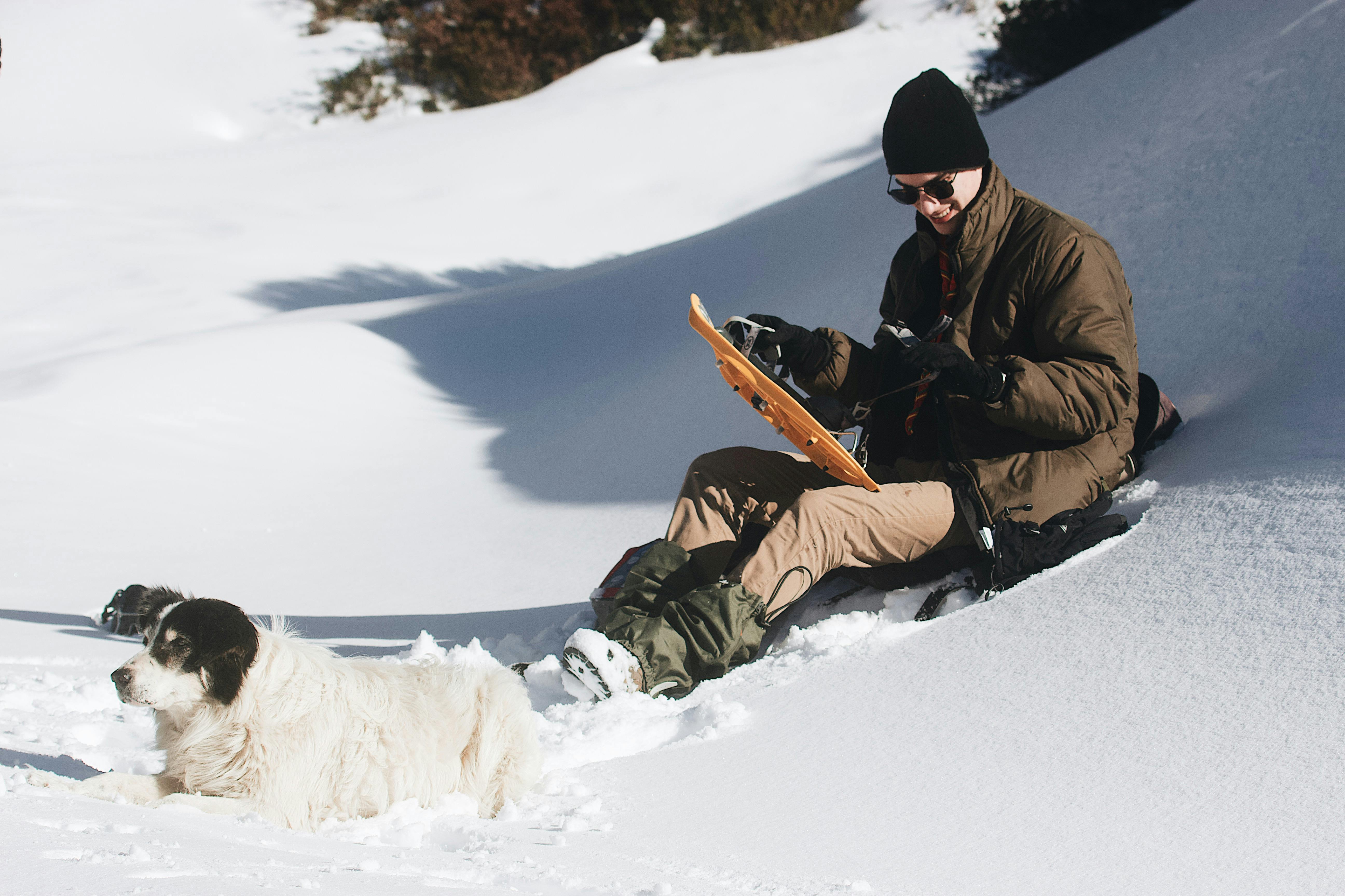 Man in Brown Jacket and Black Pants Sitting on Snow Covered Ground