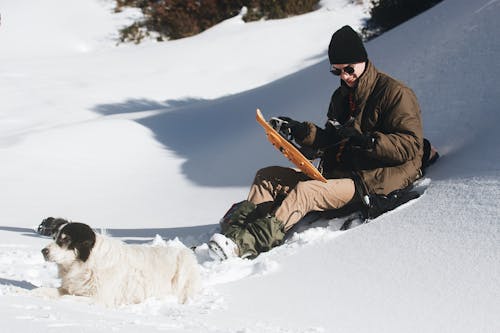 Man in Brown Jacket and Black Pants Sitting on Snow Covered Ground