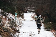 一名男子徒步穿越白雪皑皑的森林小径，拥抱冬季的冒险与自然