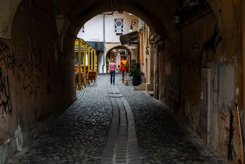 Free Picturesque cobblestone alleyway in a European city with graffiti and two people walking in the distance. Stock Photo