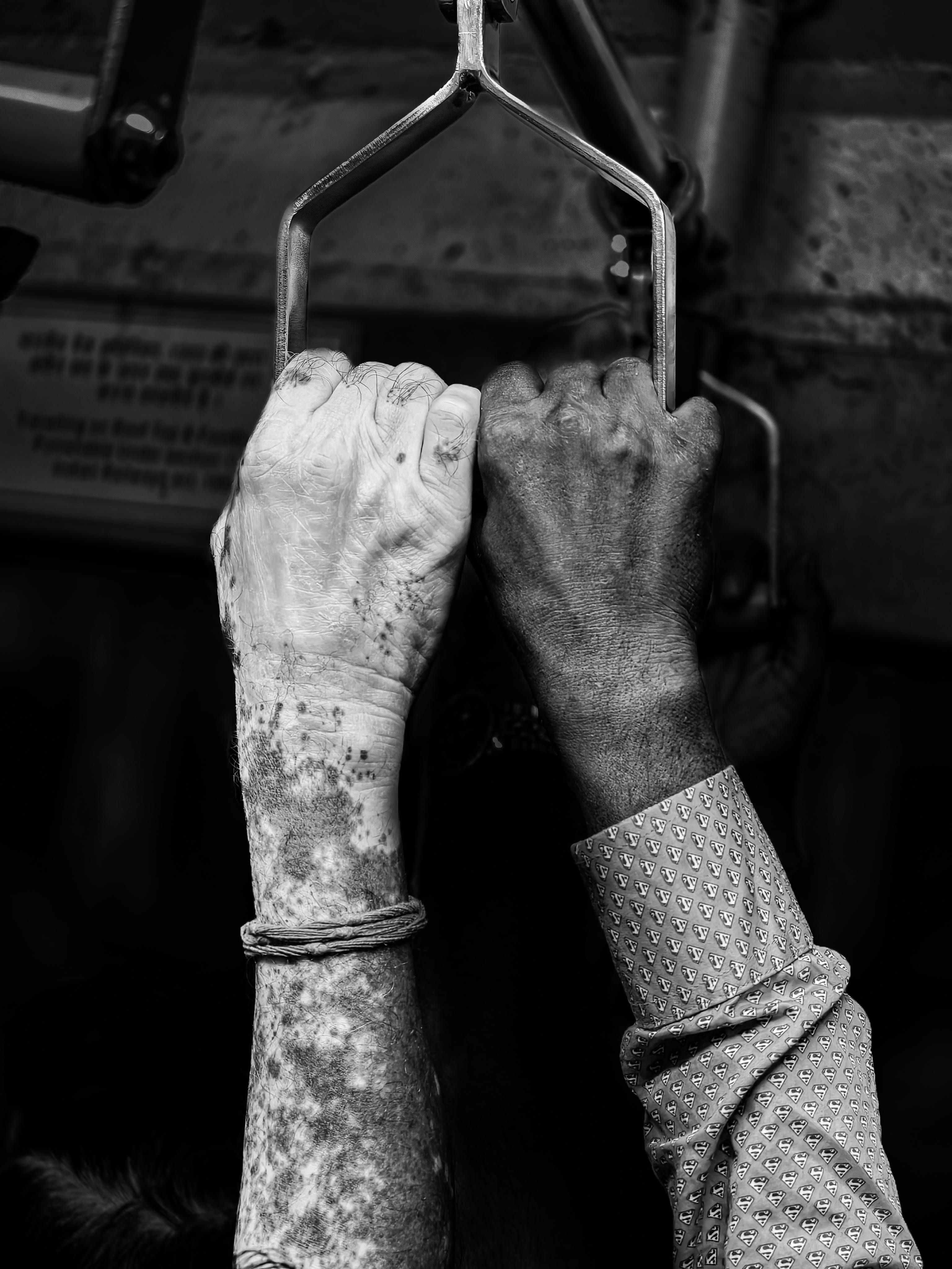 бесплатная Черно-белая фотография, на которой изображены разные руки, держащиеся за поручни в метро, ​​символизирующие единство. Стоковое фото