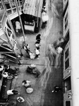 A black and white aerial view capturing bustling motion on a railway platform with passengers boarding.