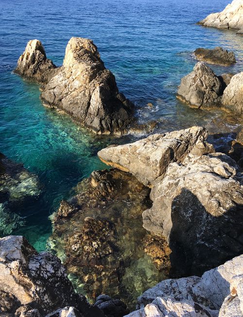 Free A breathtaking view of rocky cliffs and pristine blue water at a sunny coastal location. Stock Photo