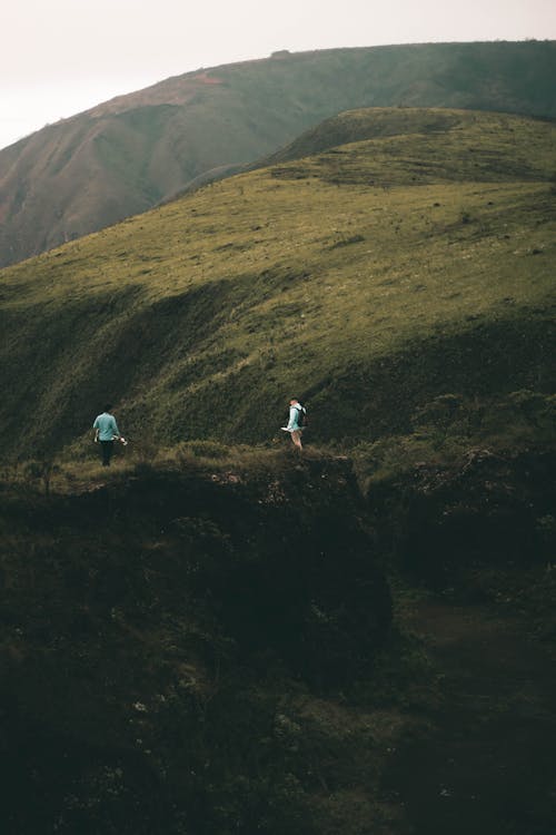 бесплатная 2 человека, стоящие на поле зеленой травы возле горы Стоковое фото